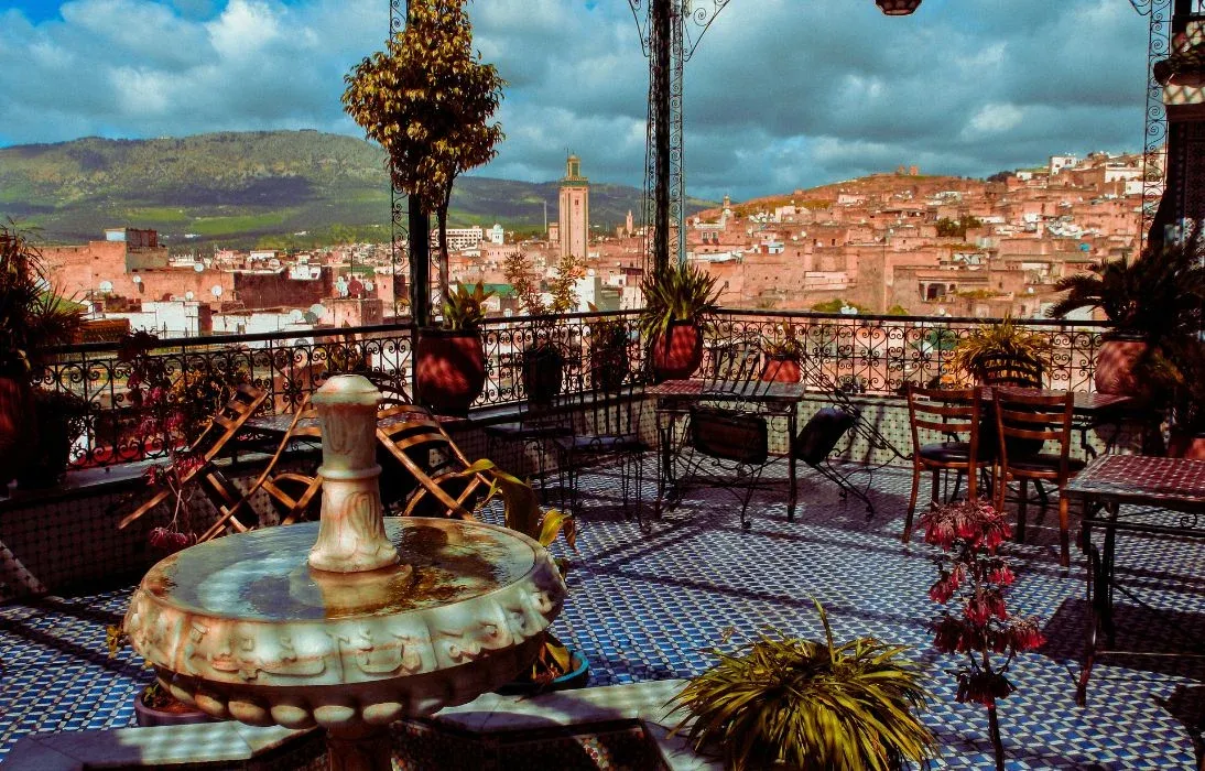 Terrasse de riad avec fontaine et zelliges bleus, vue sur une médina et ses collines